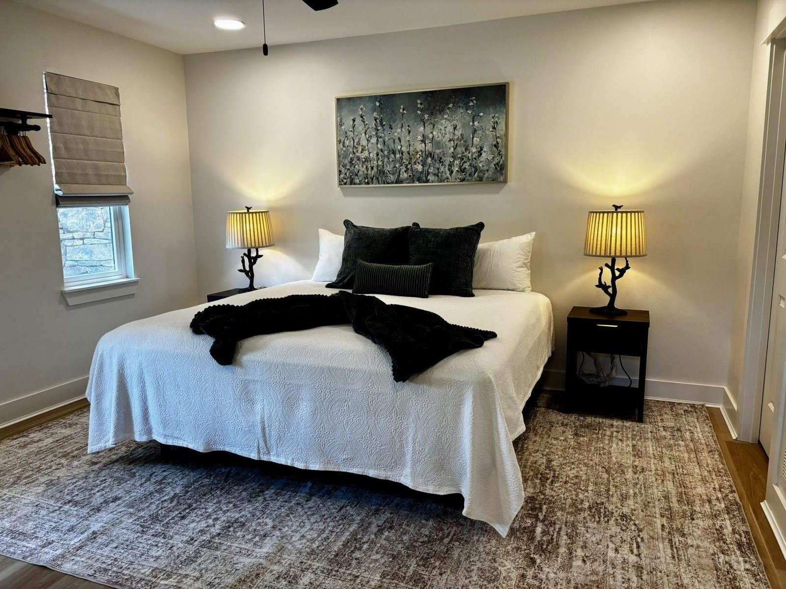 The downstairs bedroom with a king bed, two lamps, a ceiling fan and a hanging rack