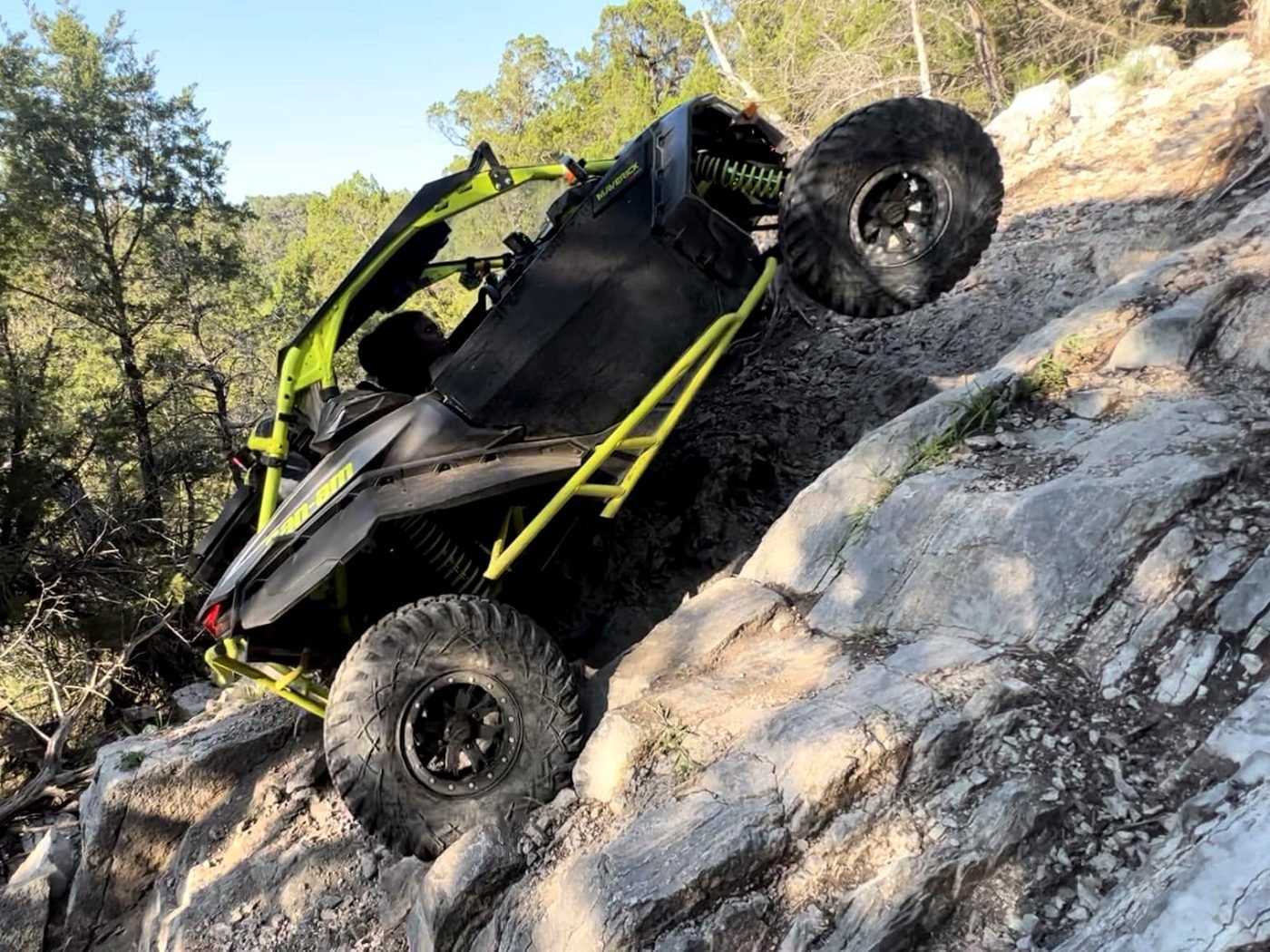 A side-by-side UTV climbing a steep rock ledge on a Cross Bar Ranch trail, front wheel lifted off the stone