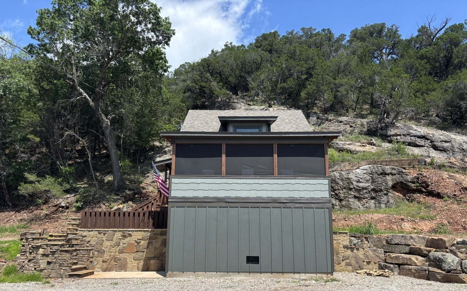 The cabin from the parking area below — green board-and-batten siding, a screened upper porch, and stone retaining walls against the hillside