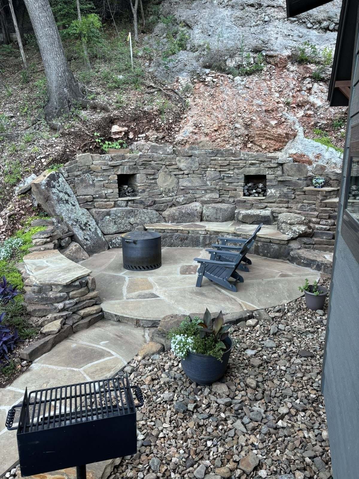 Looking down on the firepit terrace: a circle of flagstone, a smokeless firepit, an Adirondack chair, and a curved stone bench