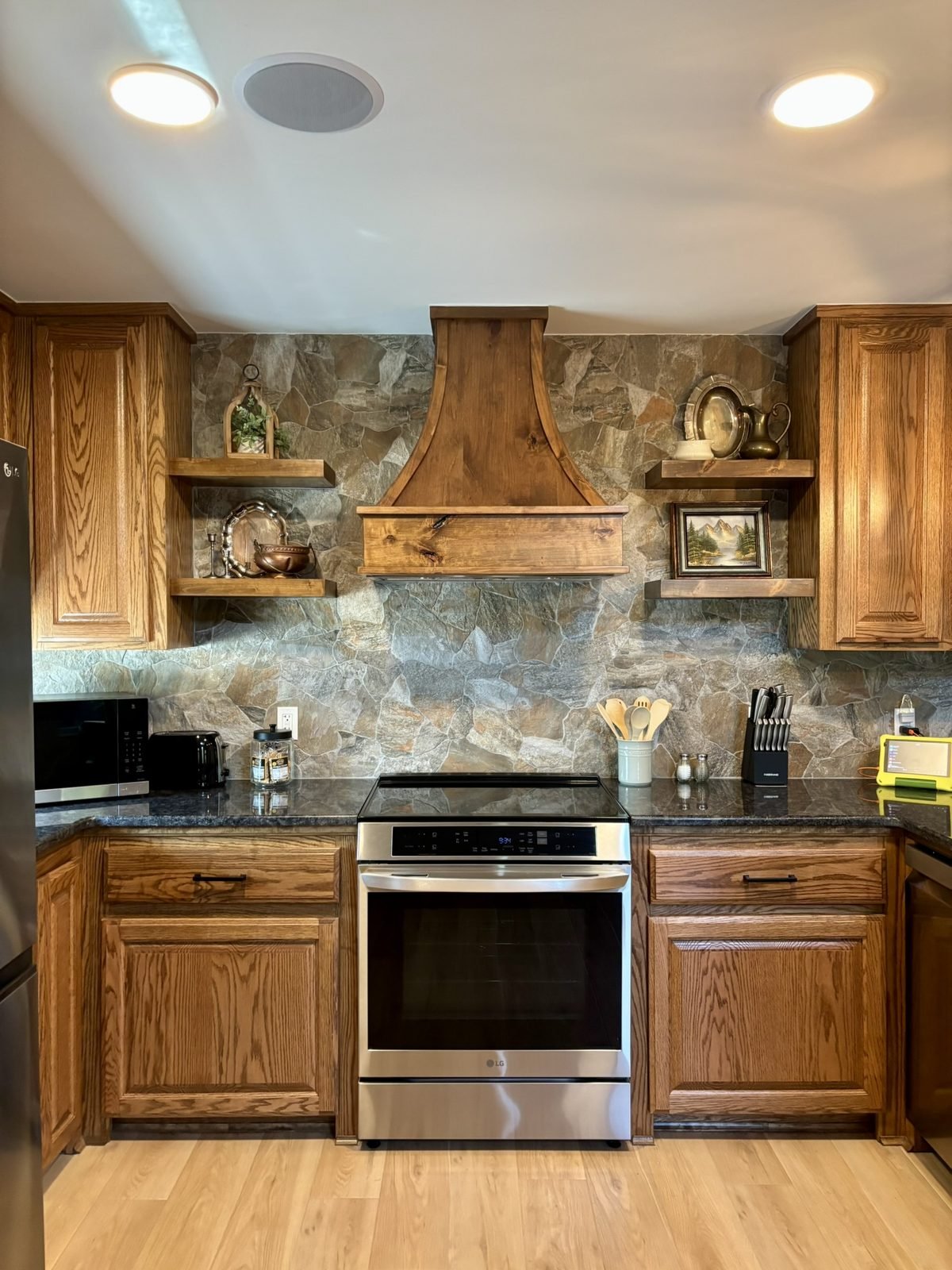 The kitchen with a stone backsplash, wooden range hood and induction range