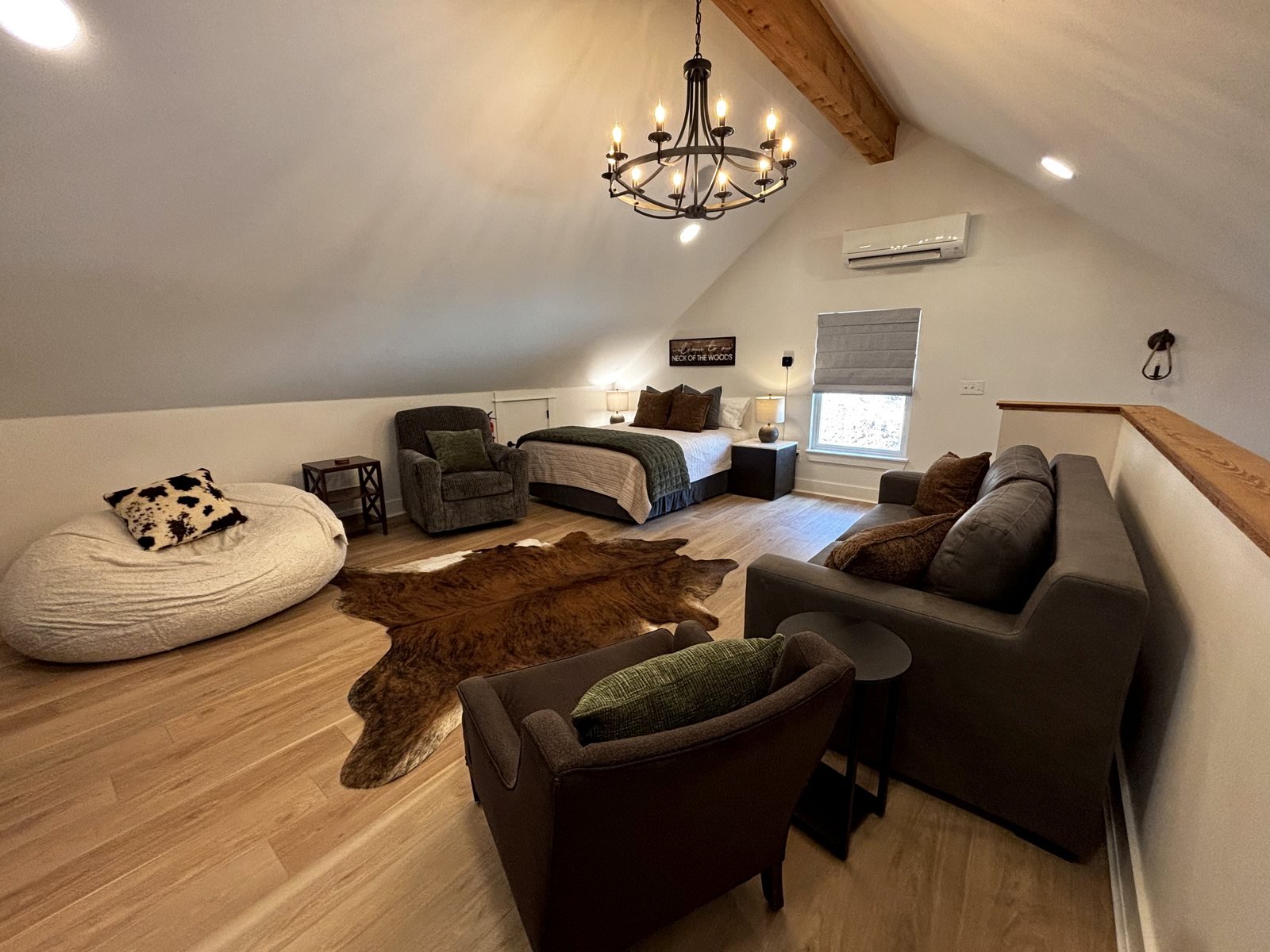 The upstairs loft: a queen bed under the vaulted ceiling with an exposed beam, an armchair, a beanbag and a sofa along the stair rail