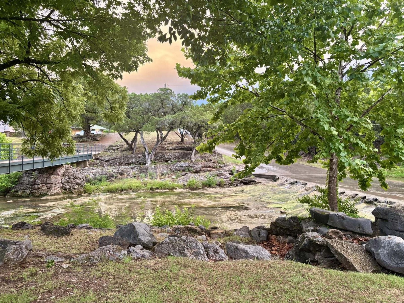 Honey Creek at dusk, running past rocks and low trees with an orange sky behind