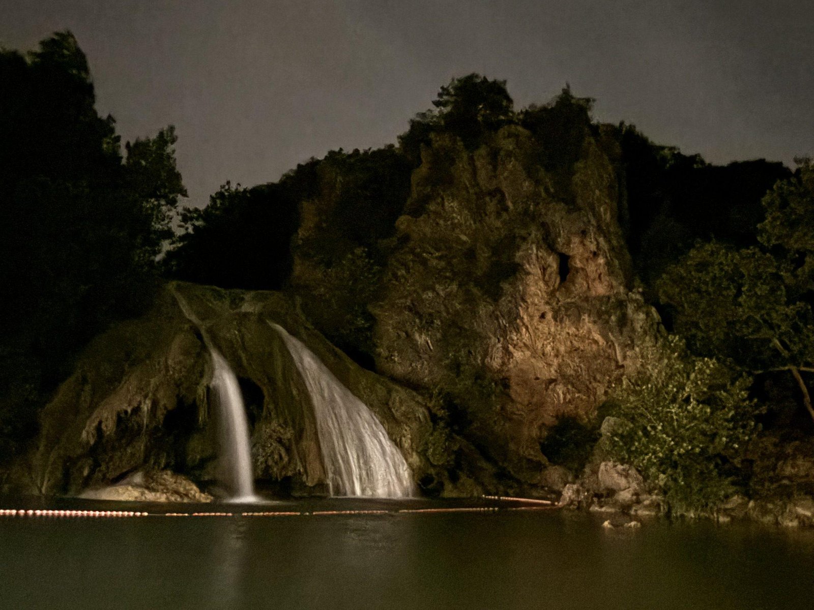 Turner Falls lit at night, water dropping into the pool below the cliff