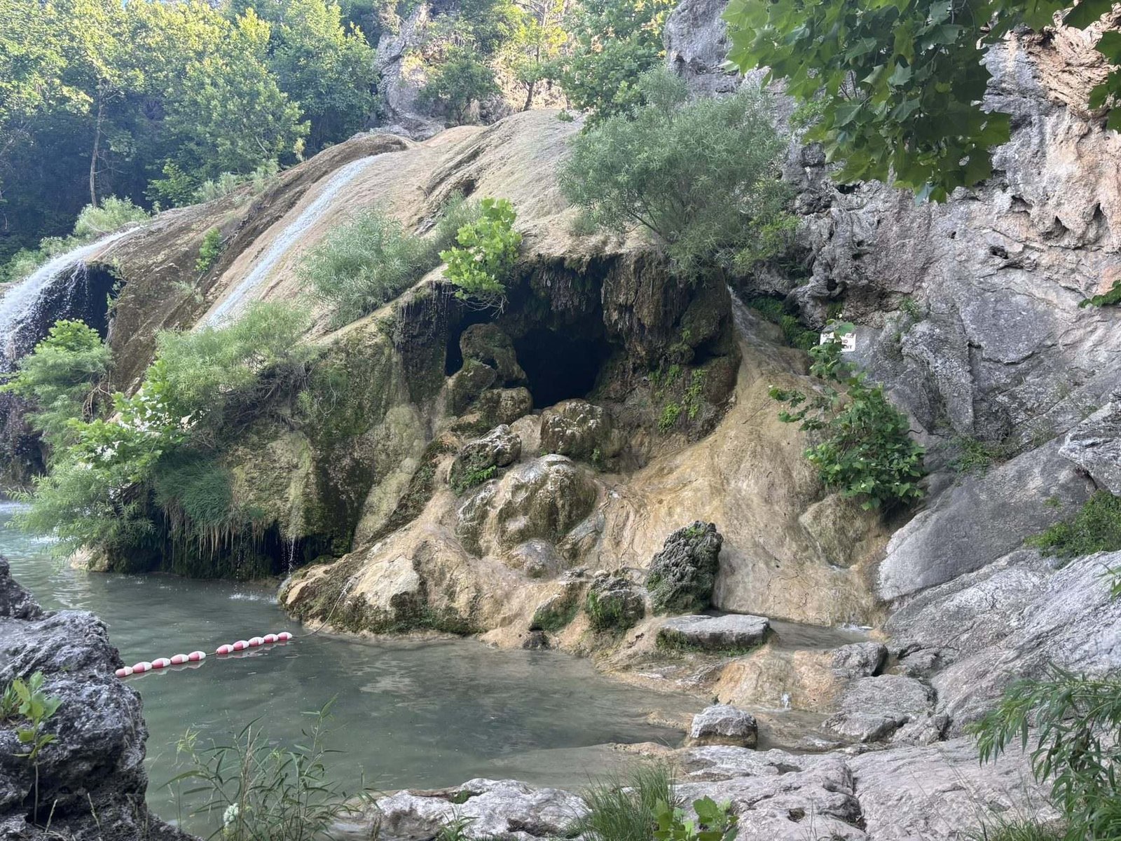 A cave opening in the rock beside the water in Turner Falls Park
